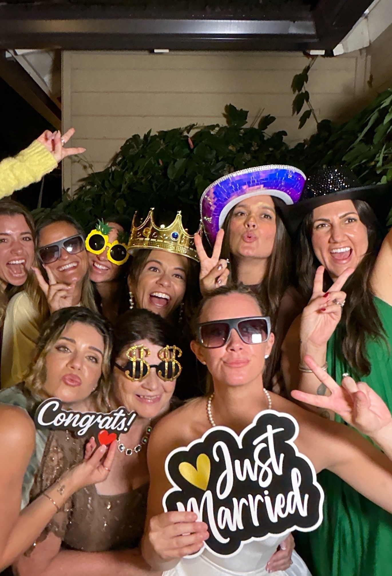 Bride and wedding guests posing with a Just Married photo booth prop